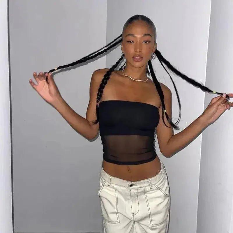 Woman in black sheer crop top and white pants, styling long braids — trendy women's fashion