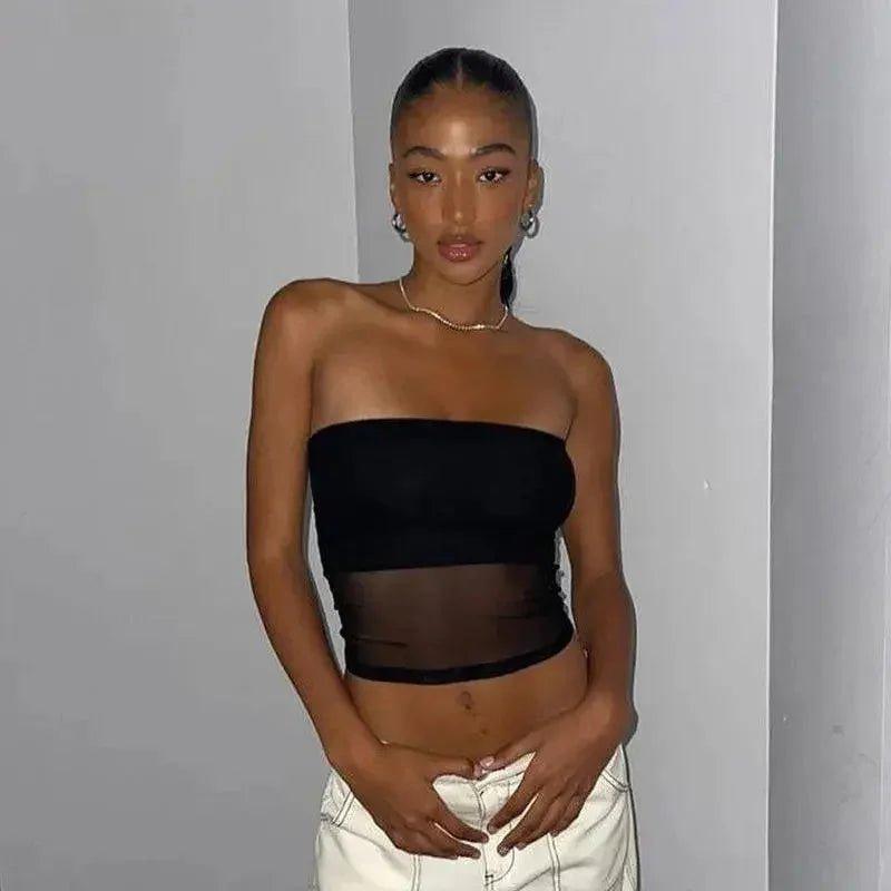 Woman wearing black strapless crop top with sheer panel, white jeans, gold necklace, and hoop earrings