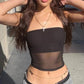 Woman in black strapless crop top with sheer panel, gold cross necklace, and waist chain, fashion style