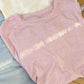 Soft pastel women's crewneck t-shirts in pink, cream, and gray, folded on wooden surface