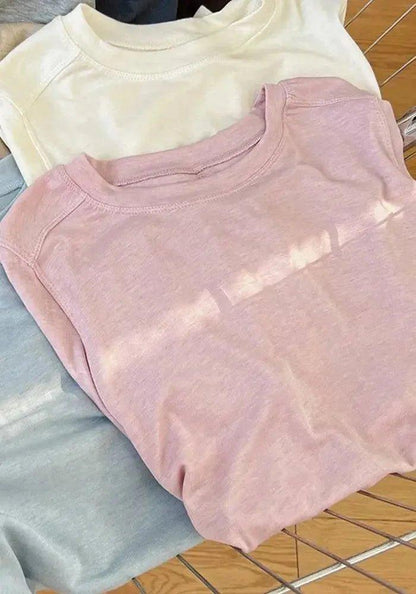Soft pastel women's crewneck t-shirts in pink, cream, and gray, folded on wooden surface