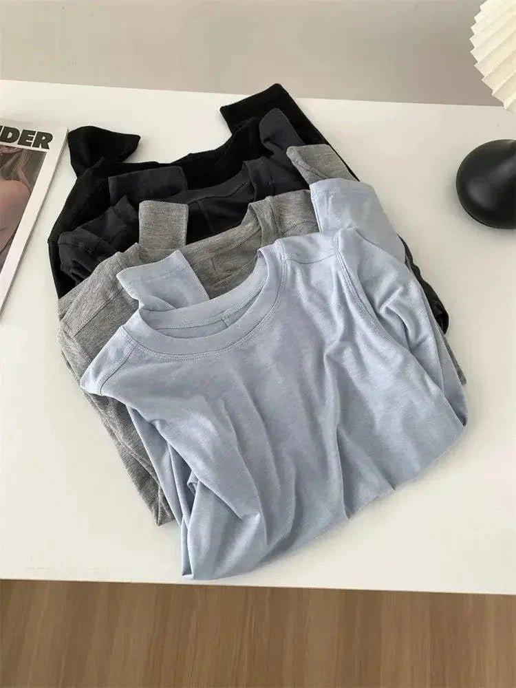 Women's basic long sleeve tops in black, gray, and light blue, folded on white table for fashion styling
