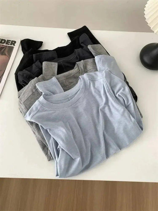 Women's basic long sleeve tops in black, gray, and light blue, folded on white table for fashion styling