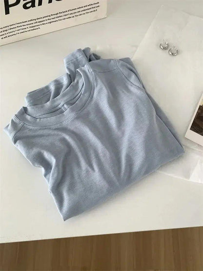 Light blue women's fashion t-shirt with minimalist styling, paired with hoop earrings and a book