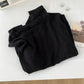 Black women's fashion top with high neck, styled with earrings and magazine on white surface