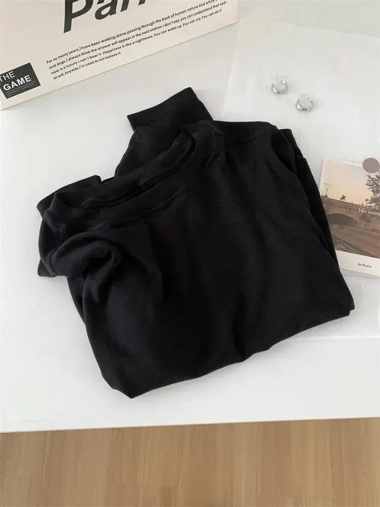 Black women's fashion top with high neck, styled with earrings and magazine on white surface