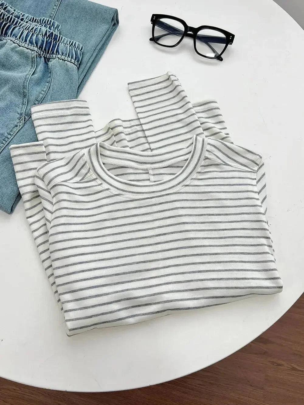 Striped women's t-shirt with denim shorts and black glasses on white table