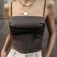 Woman wearing stylish brown corset top with layered gold necklaces and white pleated pants