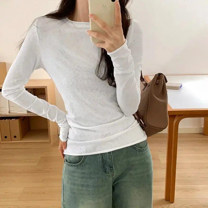 Woman wearing white long sleeve top with ruched hem, paired with green jeans, holding phone and brown bag