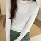 White long sleeve women's fashion top with layered design, paired with green jeans for casual style