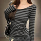 Woman wearing gray and black striped long sleeve top with off-shoulder neckline, paired with jeans