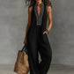 Woman in black sleeveless jumpsuit with white embroidery, holding woven tote bag, fashion outfit