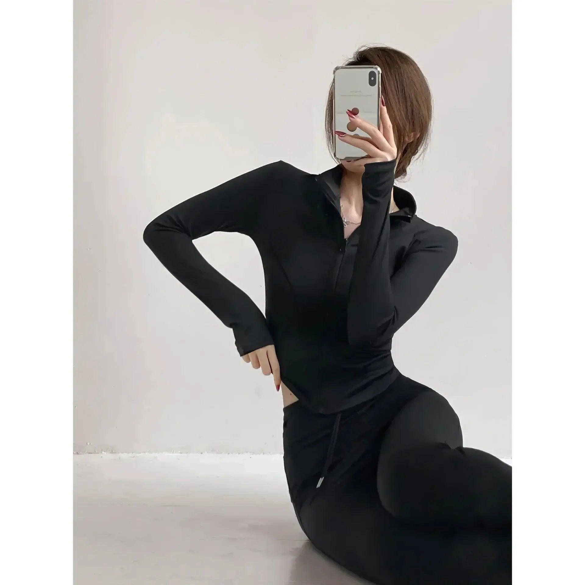 Woman in black long sleeve zip-up top and leggings, taking mirror selfie for fashion look
