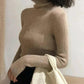 Woman wearing beige ribbed turtleneck sweater with cozy knit texture, styled with black pants and cream tote bag