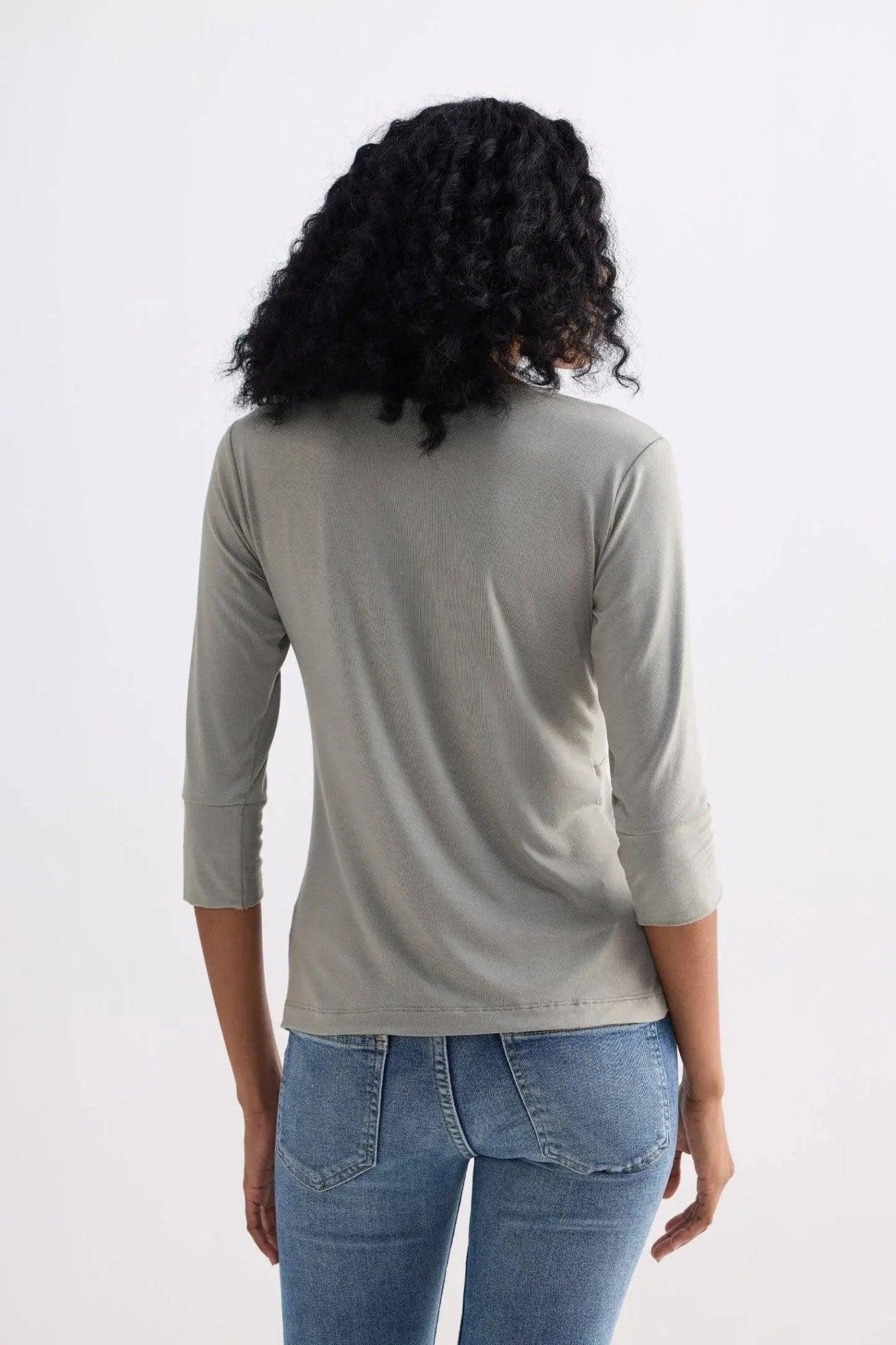 Woman wearing olive green ribbed 3/4 sleeve top with blue jeans, back view