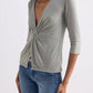 Woman wearing olive green wrap top with twist front, 3/4 sleeves, paired with blue jeans for casual fashion