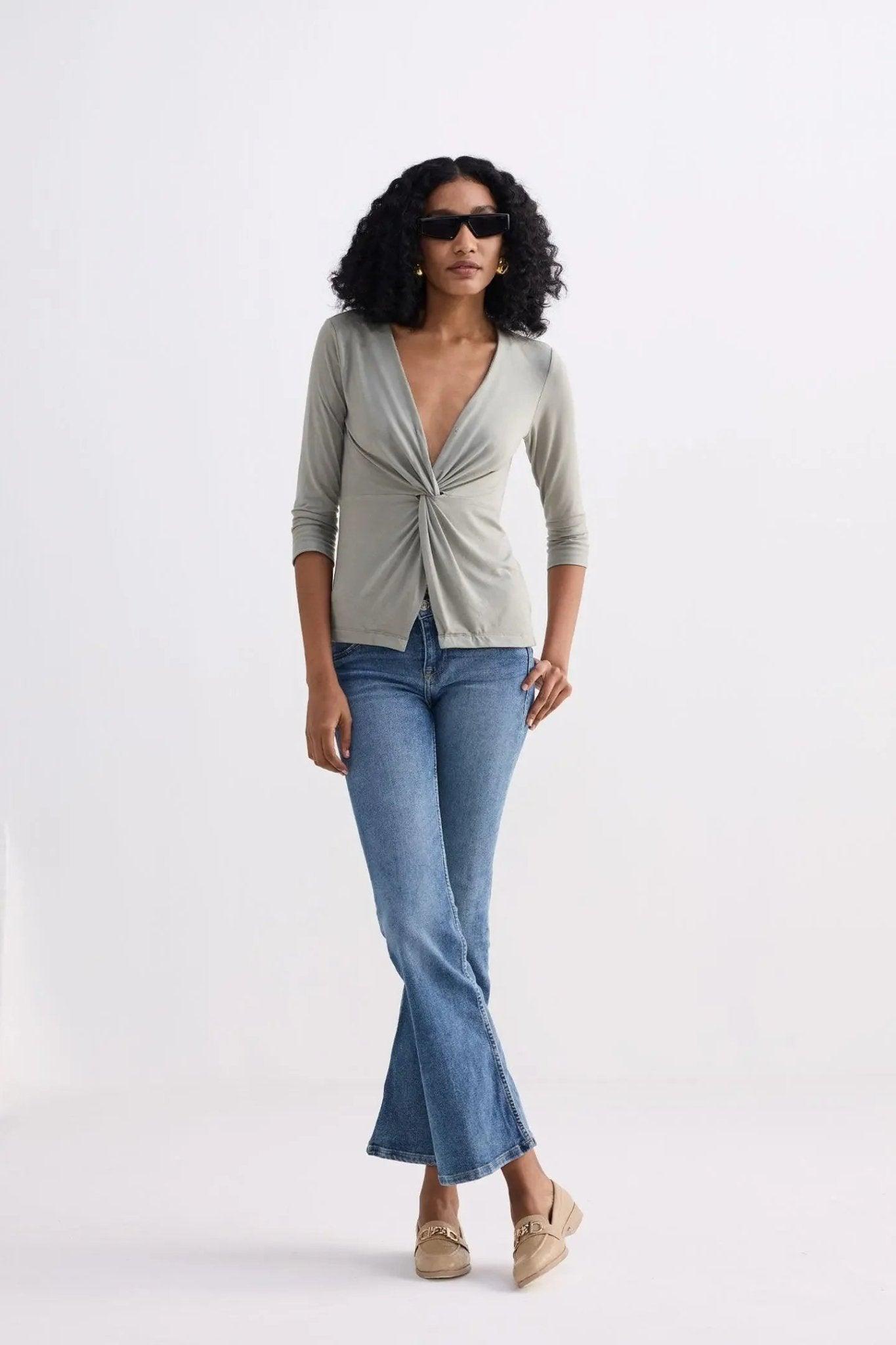 Woman in olive green twist-front top, blue flare jeans, and beige loafers for stylish fashion look
