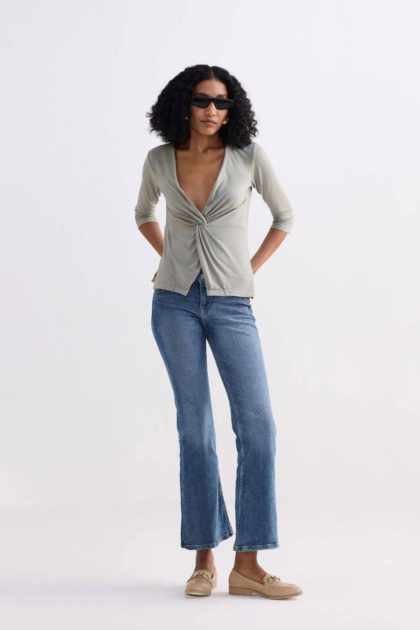 Woman in olive twist-front top, blue flare jeans, and beige loafers, stylish fashion outfit