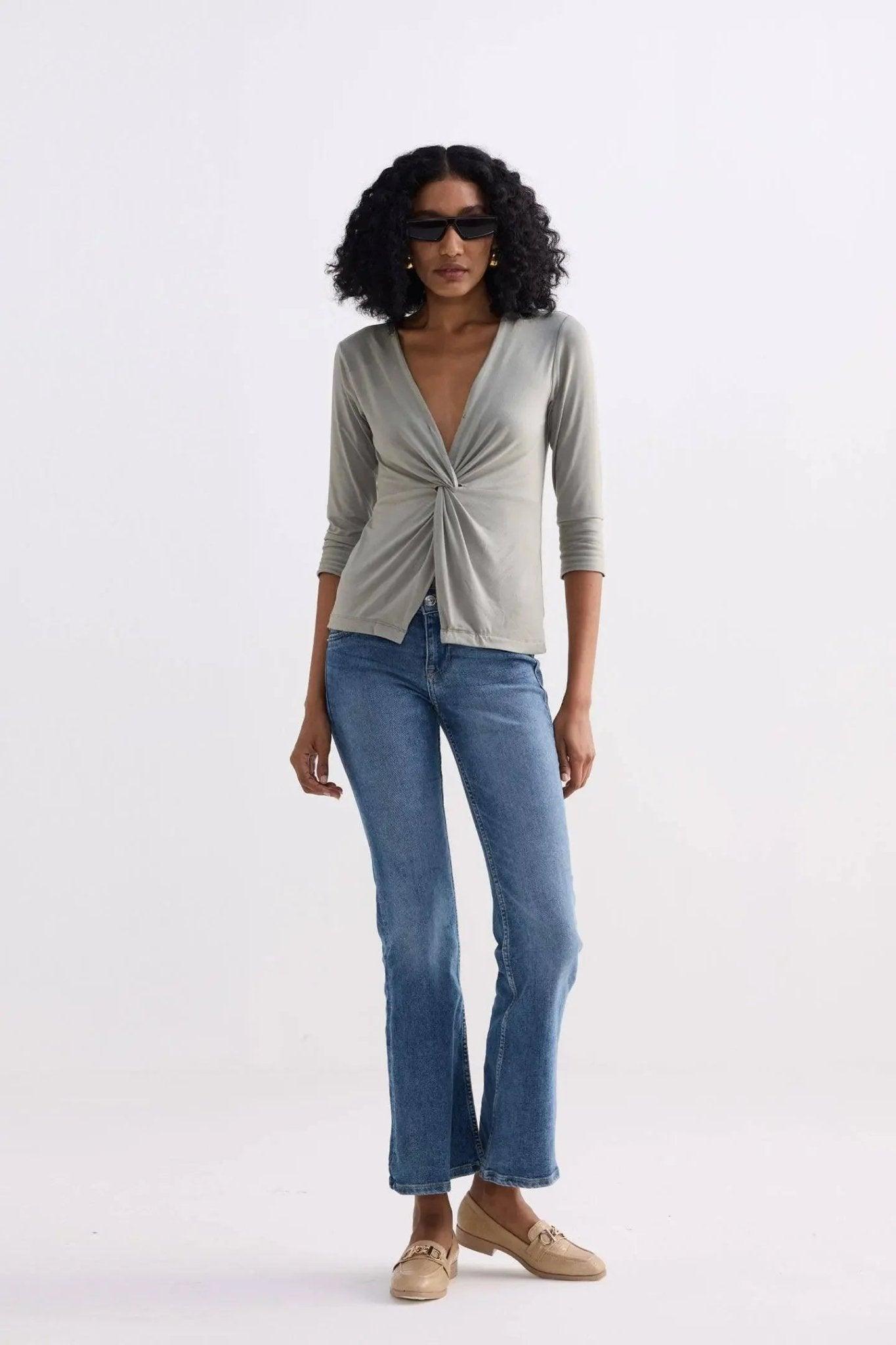 Woman wearing olive twist-front top, blue flared jeans, and beige loafers for casual fashion look