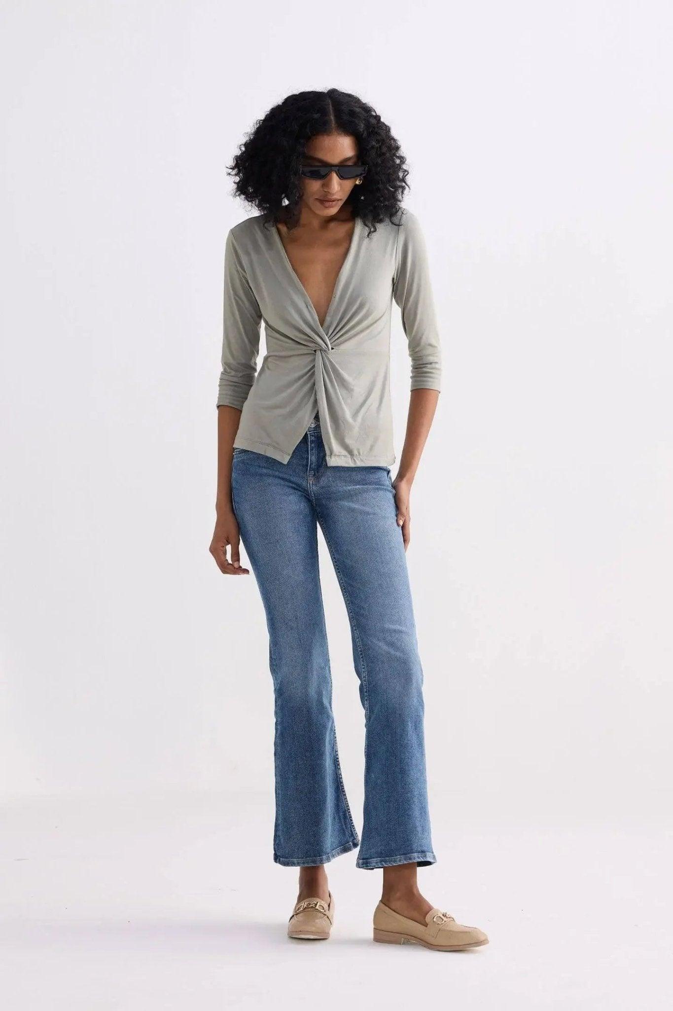 Woman in olive twist-front top, blue flare jeans, and beige loafers — stylish women's fashion outfit