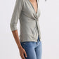 Woman wearing olive green wrap top with twist front, 3/4 sleeves, paired with blue jeans