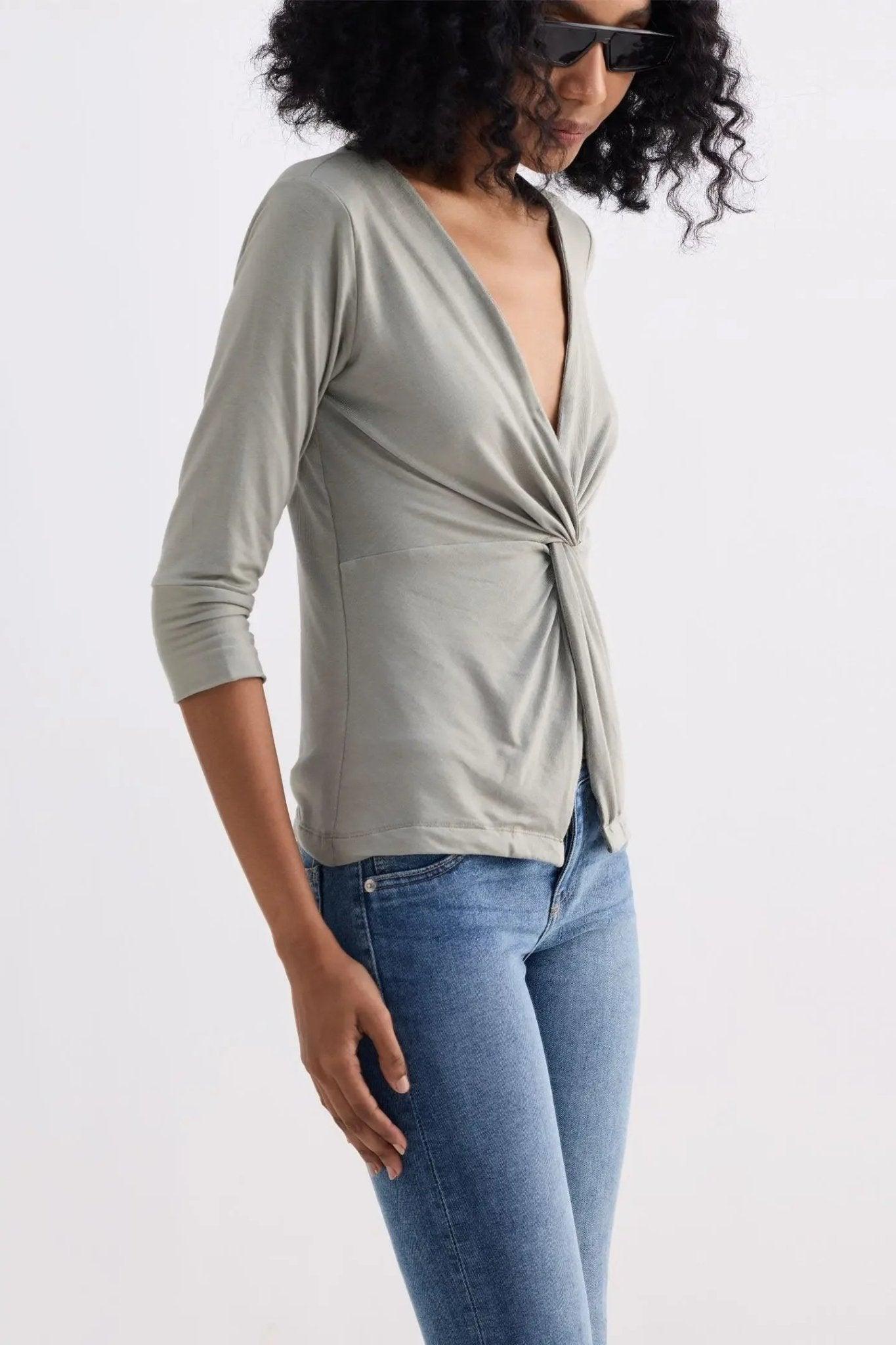 Woman wearing olive green wrap top with twist front, 3/4 sleeves, paired with blue jeans