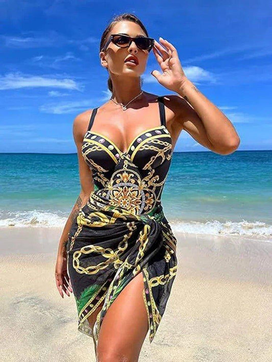 Woman in stylish black and gold chain print beach dress with high slit, sunglasses, ocean backdrop