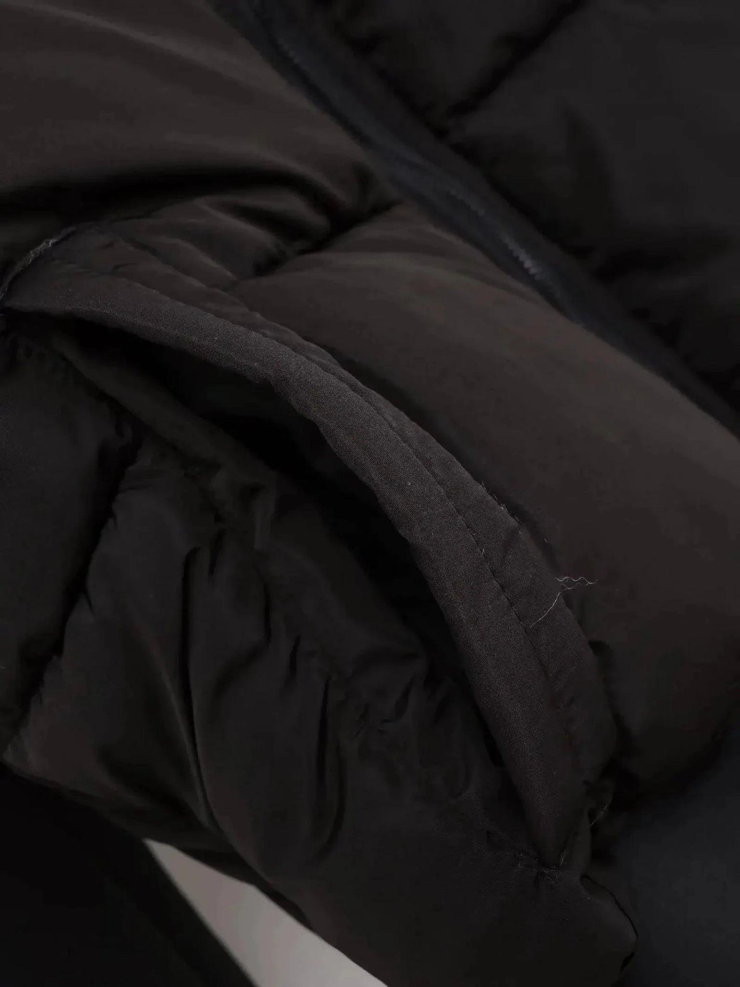 Black puffer jacket close-up showing quilted texture and zipper detail, women's fashion outerwear