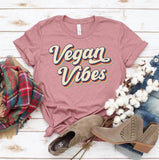Pink 'Vegan Vibes' graphic tee with plaid scarf, denim, cotton stems, and suede boots on wood