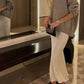 Woman in gray oversized sweater and white flowy pants, holding black clutch, stylish fashion outfit