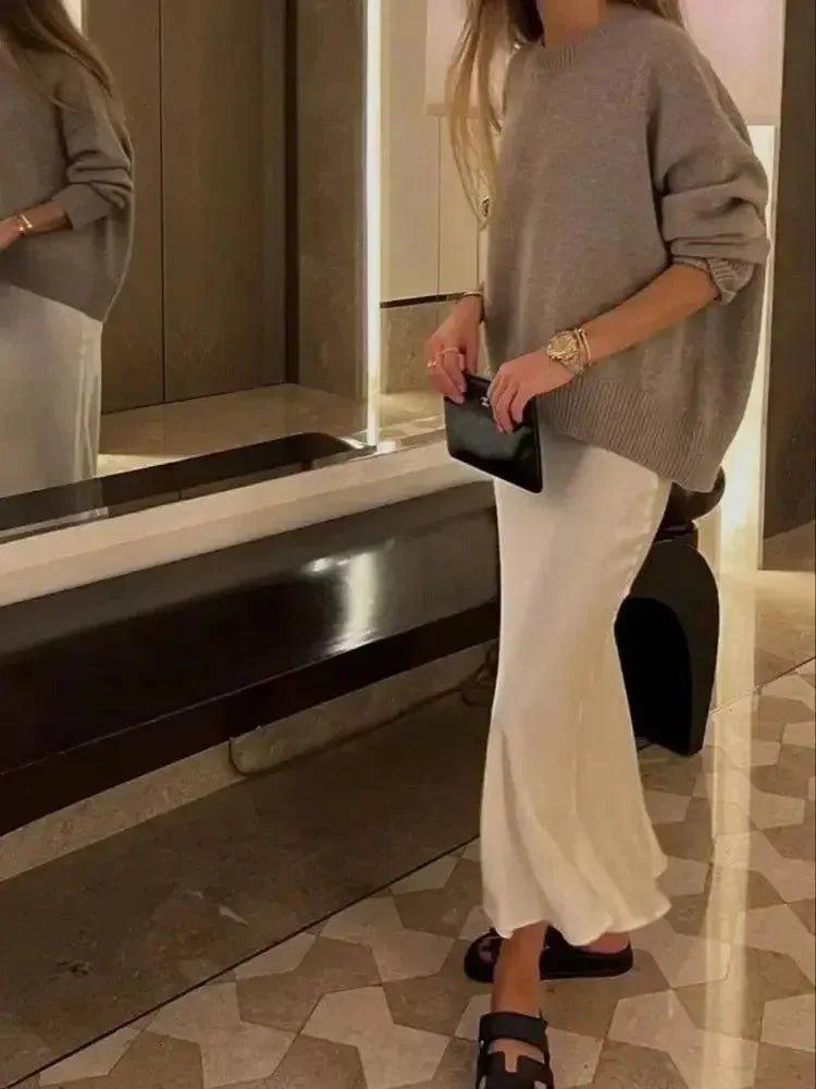 Woman in gray oversized sweater and white flowy pants, holding black clutch, stylish fashion outfit