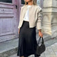 Woman in beige bomber jacket, black midi skirt, white sneakers, and sunglasses, holding black handbag