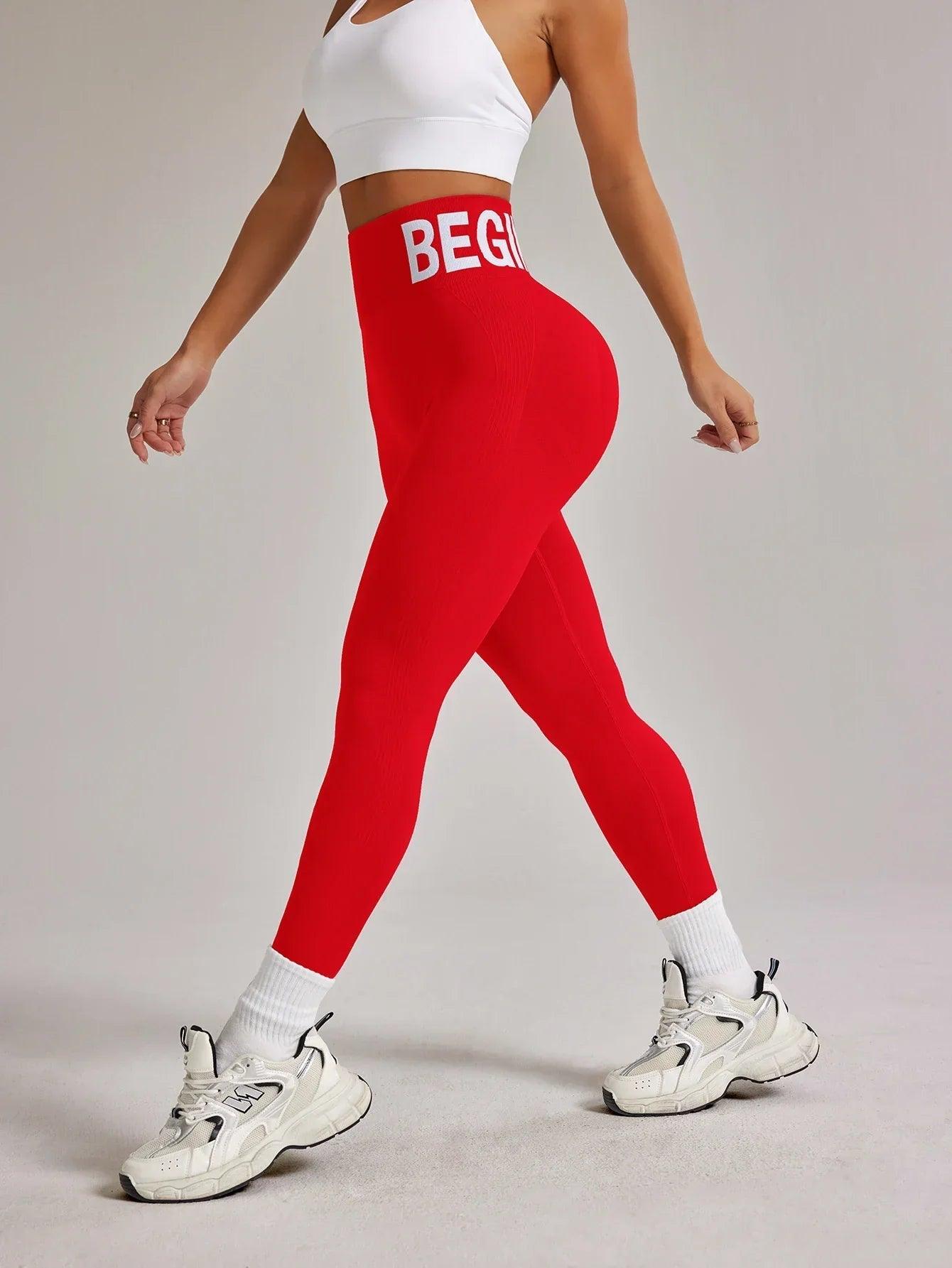 Woman in red high-waist leggings with 'BEGIN' waistband, white sports bra, and chunky sneakers