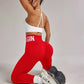 Woman in red high-waist leggings with 'BEGIN' print, white sports bra, and sneakers, fitness fashion
