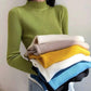 Woman in green ribbed turtleneck sweater holding stack of colorful knit tops, women's fashion