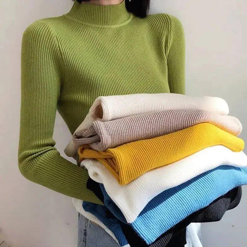 Woman wearing olive green ribbed turtleneck sweater holding stack of colorful knit tops