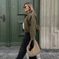 Woman in olive corduroy jacket, black jeans, and woven bag walking past green door — stylish street fashion