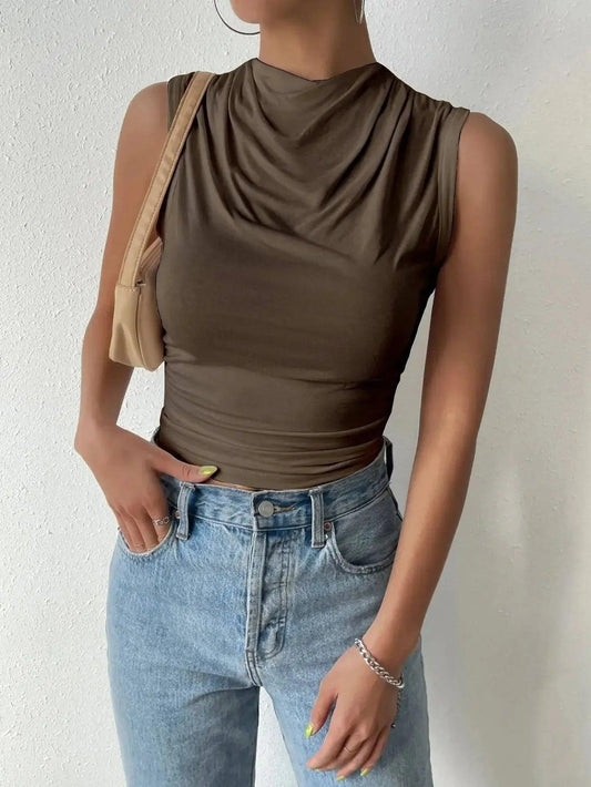 Woman wearing olive green cowl neck sleeveless top with light wash jeans and beige shoulder bag