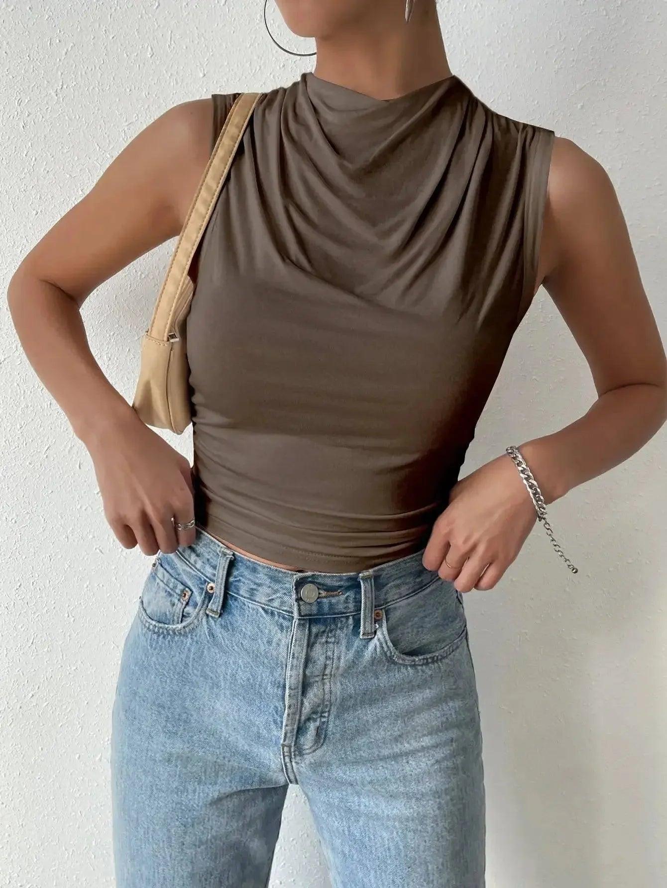 Woman wearing olive green cowl neck sleeveless top with light wash jeans and tan shoulder bag