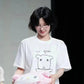 Woman wearing cute white graphic tee with cartoon bear, holding pink plush toy, stylish short hair and glasses