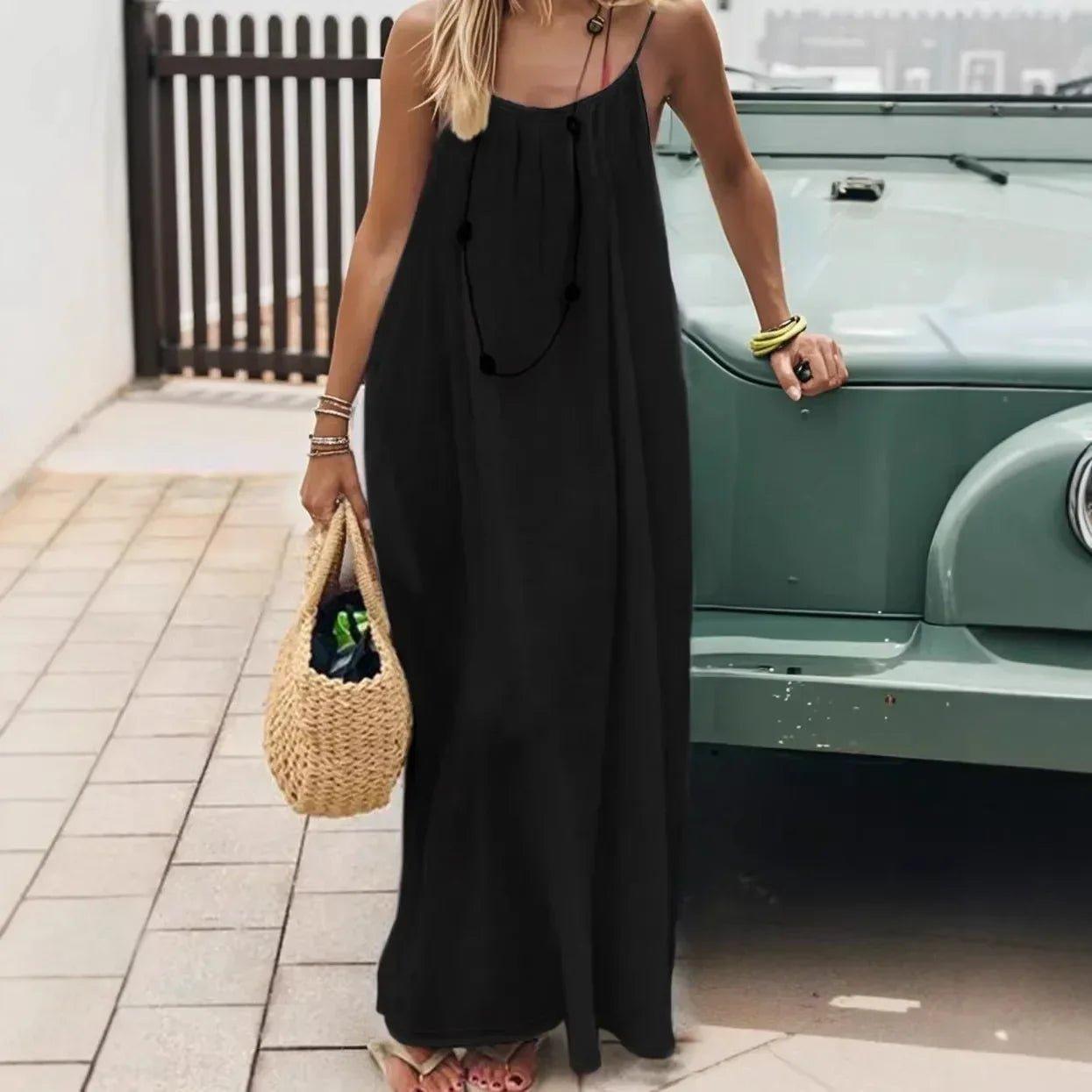 Woman in black spaghetti strap maxi dress with straw bag, standing by vintage car