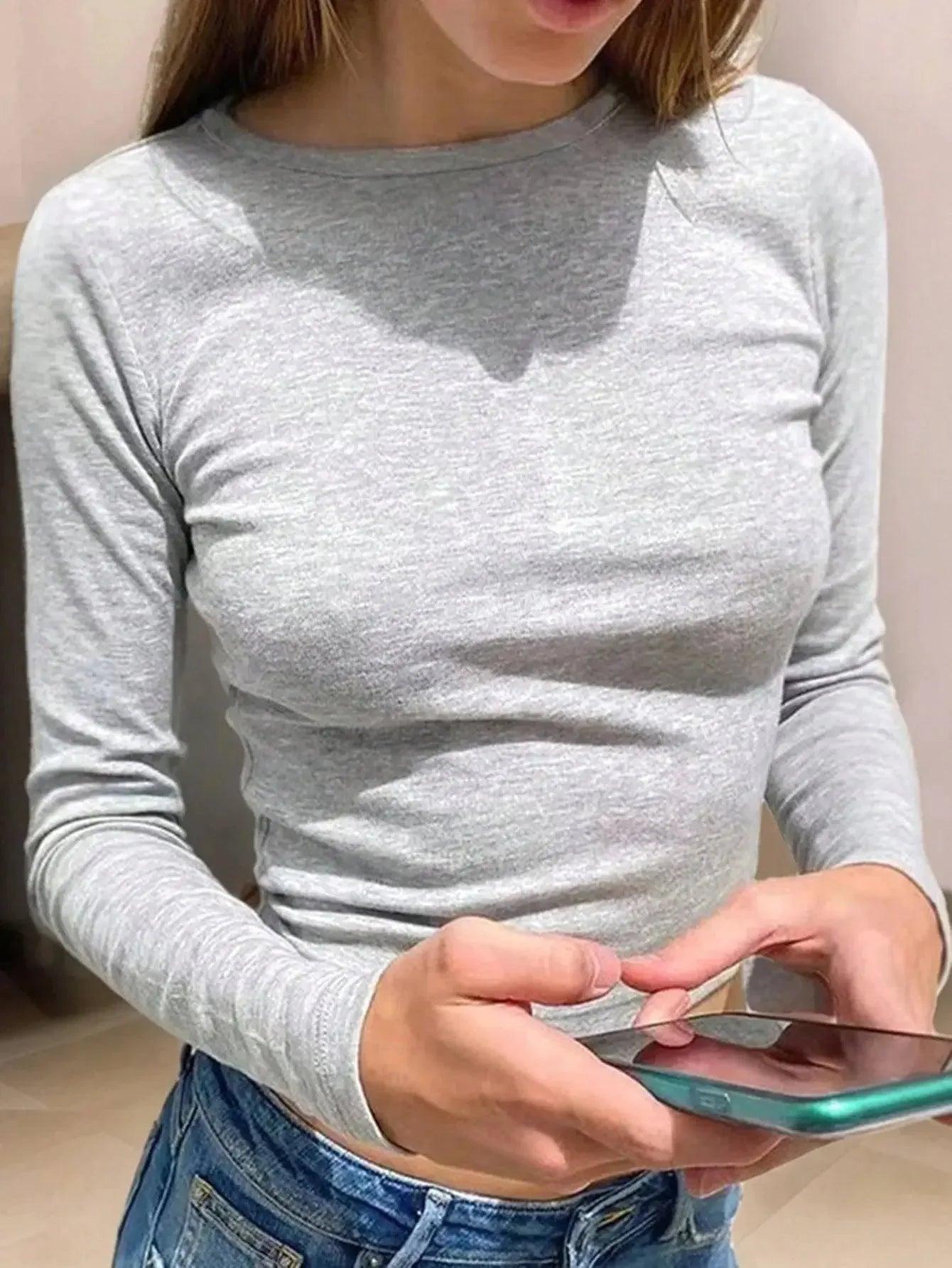 Woman in gray long sleeve top and jeans holding phone, casual fashion outfit