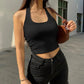 Woman in black ribbed crop top and high-waisted jeans, holding brown crossbody bag, street fashion style