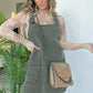 Woman in olive green denim overall dress with sheer lace top and chain strap bag, fashion style