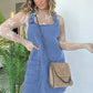 Woman in blue denim overall dress with lace top and chain strap bag, stylish fashion outfit