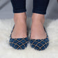 Blue and black patterned women's flats with white stitching, worn with rolled jeans on fluffy rug