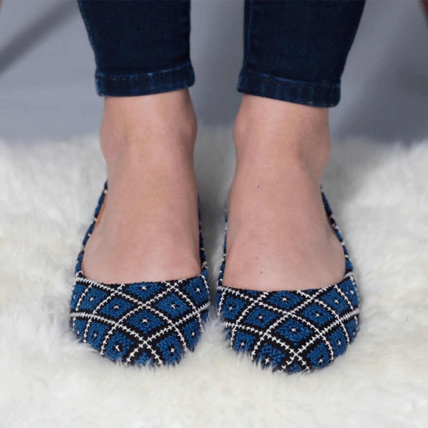 Blue and black patterned women's flats with white stitching, worn with rolled jeans on fluffy rug