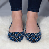Blue and black patterned women's flats with white stitching, worn with rolled jeans on fluffy rug