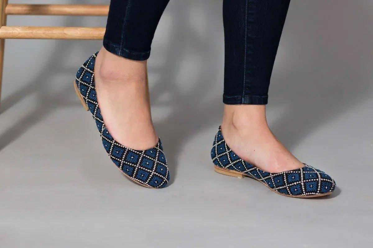 Blue patterned flat shoes with white embroidery, worn with dark jeans, stylish women's fashion footwear