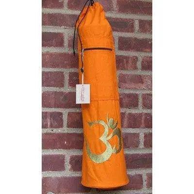 Orange yoga mat bag with gold Om symbol, hanging on brick wall, ideal for women's fitness and wellness